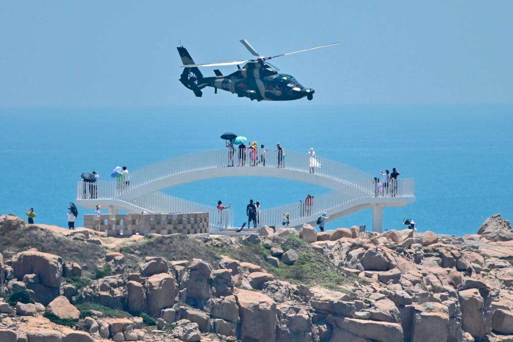 Tourists look on as a Chinese military helicopter flies past Pingtan island, one of mainland China’s closest point from Taiwan, in Fujian province/AFPPix