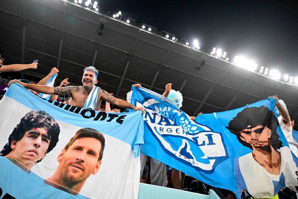 Argentina supporters wave flags depicting portraits of football legend Diego Maradona (L) and Argentina’s forward #10 Lionel Messi as they cheer after their team won the Qatar 2022 World Cup Group C football match between Poland and Argentina at Stadium 974 in Doha on November 30, 2022. AFPPIX