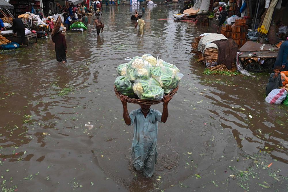 A labourer carries a basket loaded with vegetables as he wades through a flooded street after heavy monsoon rains in Lahore/REUTERSPix