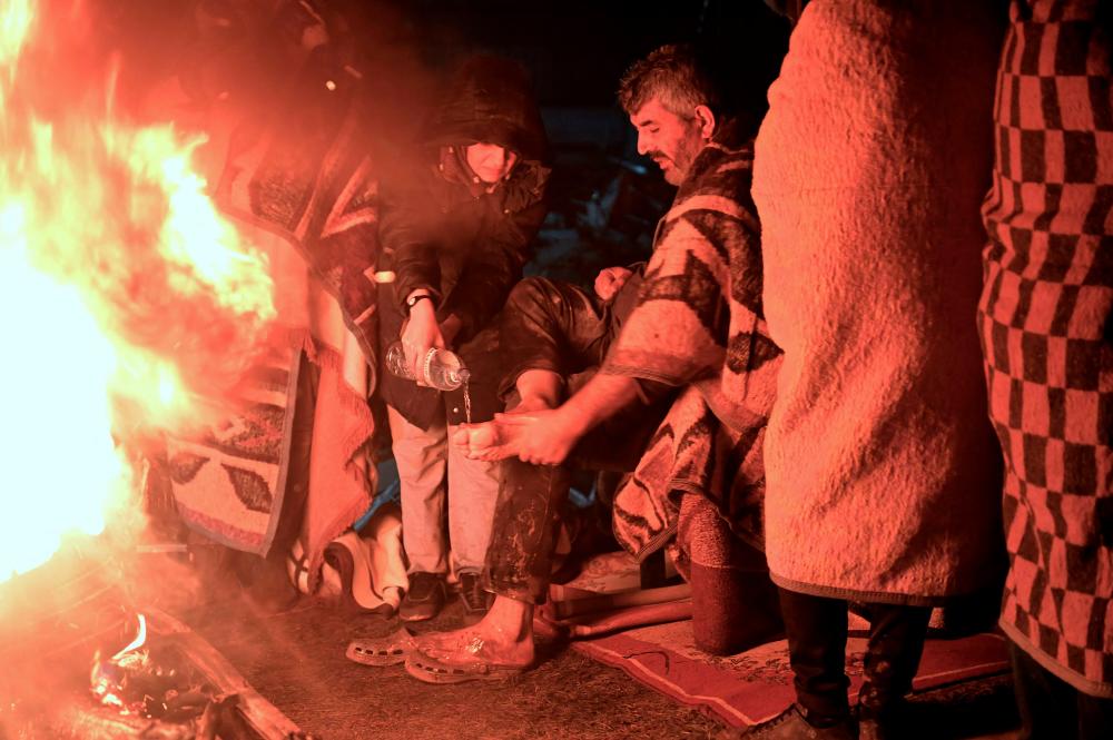 People warm themselves around a bonfire in the rubble in Kahramanmaras, Turkey, after a 7.8-magnitude earthquake struck the country’s southeast on February 7, 2023/AFPPix