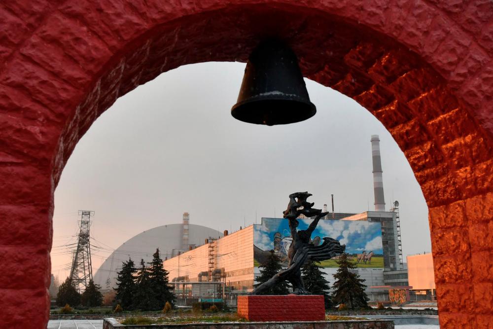 $!This photograph taken on December 8, 2020 shows a monument in front of the giant protective dome built over the sarcophagus of the destroyed fourth reactor of Chernobyl nuclear power plant. AFP / GENYA SAVILOV