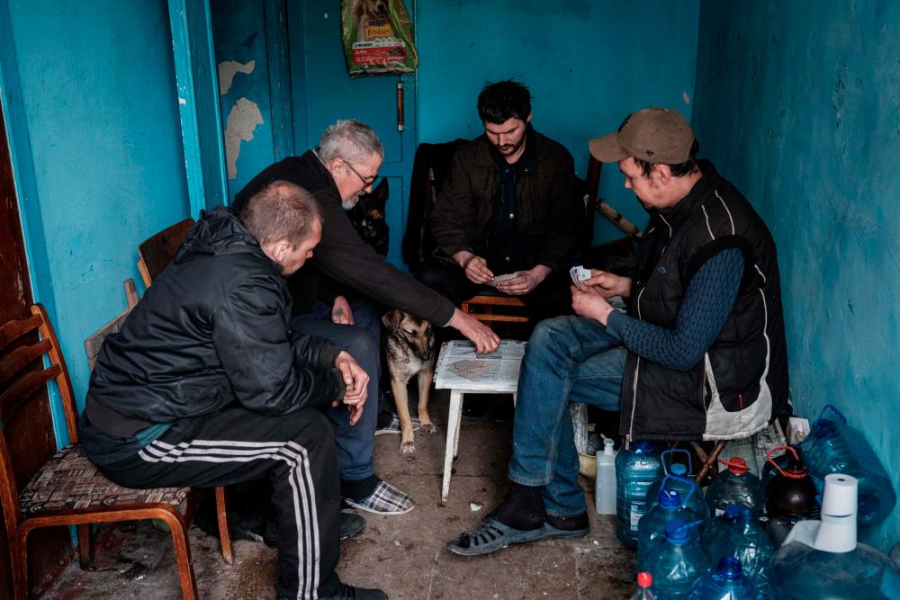 Internally displaced men play cards at the entrance of a bunker under the destroyed building of the Palace of culture in Rubizhne, eastern Ukraine, on April 23, 2022. AFPPIX