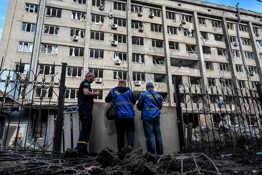 Three firemen stand in front of a destroyed building in Kramatorsk, in the Donetsk region on September 18, 2022, amid the Russian invasion of Ukraine. - AFPPIX