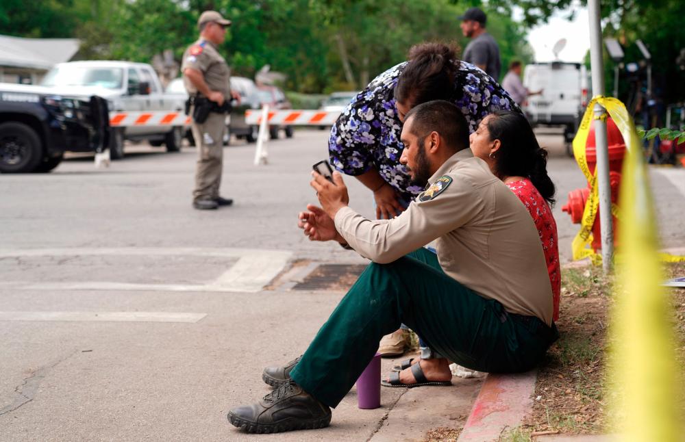 A sheriff checks his phone as he sits on the sidewalk with two women outside Robb Elementary School as state troopers monitor the area in Uvalde, Texas, May 24, 2022. AFPPIX