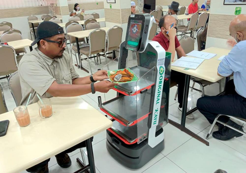 A customer picking up food delivered to him by a robot at a restaurant in Bukit Jambul, Bayan Lepas, Penang. – MASRY CHE ANI/THESUN