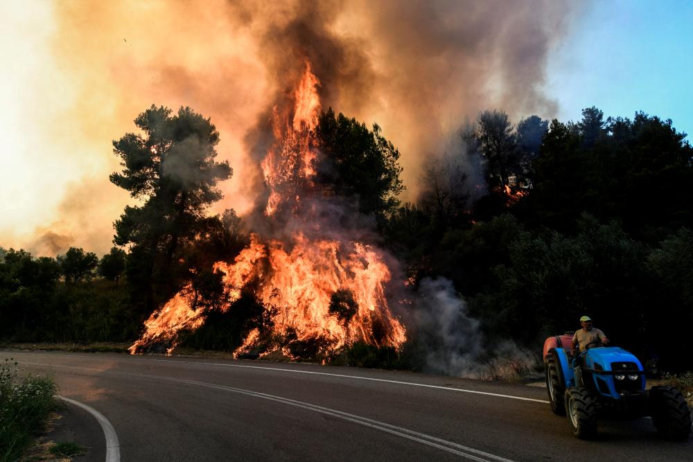 A local drives a tractor next to a wildfire burning at the village of Krestena, in the western Peloponnese, Greece. – REUTERSPIX